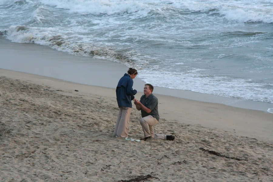 Discover the heartwarming engagement story of Natalie and her partner by the beach. Read how a surprise proposal unfolded with a scenic sunset backdrop.