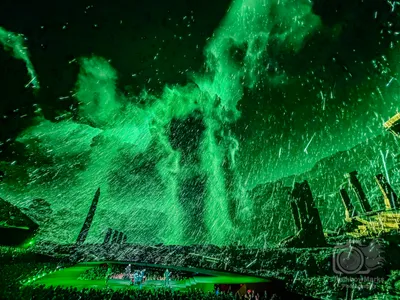 A green storm sweeps over ancient ruins above the stage